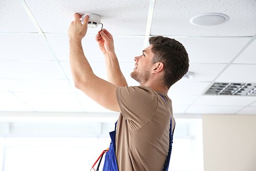 electrician installing smoke detector on ceiling